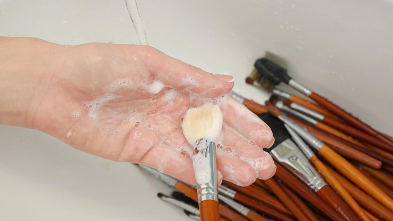 Manos limpiando pinceles de maquillaje
