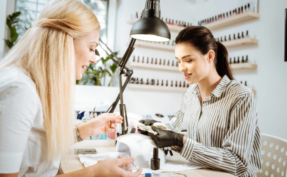 Mujer dando opciones de uñas a una cliente previo a la realización de un manicure