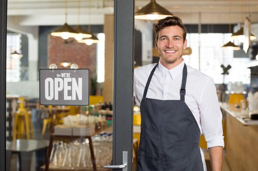 hombre al lado de un letrero 'open' en su restaurante