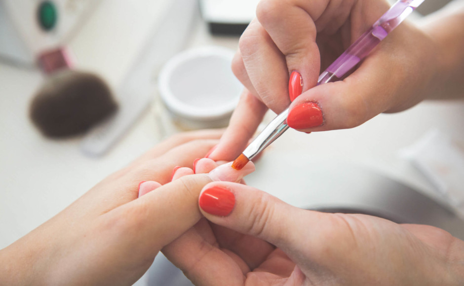 Mãos de uma mulher aplicando unhas de gel em uma cliente