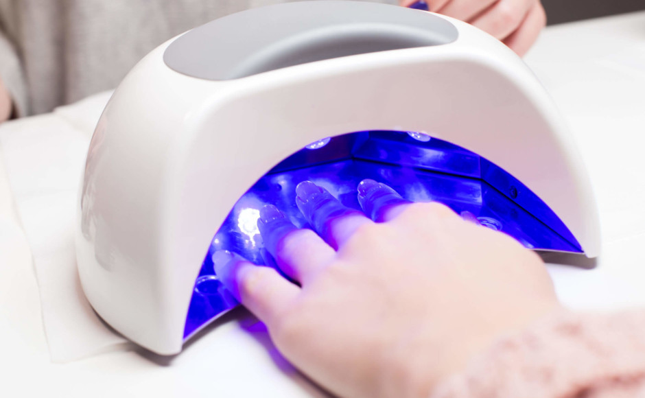 Mãos de uma mulher com a mão em um dispositivo para fazer unhas de gel