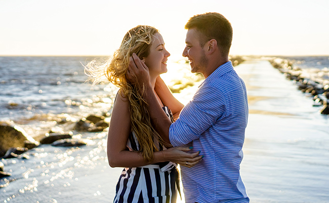 foto de una pareja caminando por una playa desierta, tomados de la mano y mirándose con expresiones felices