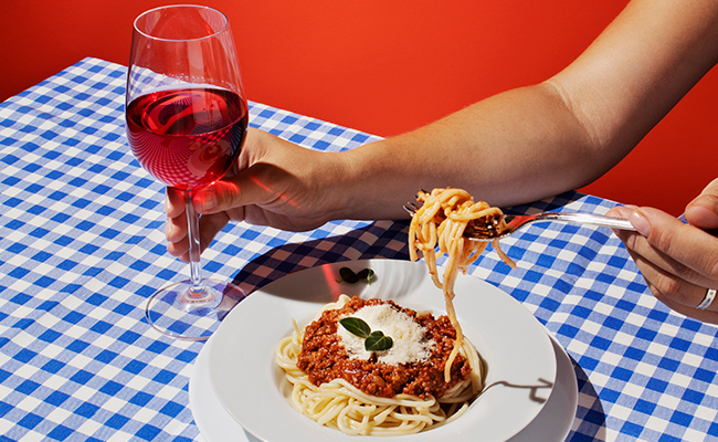 Copa de vino con un plato de fideos con bolognesa