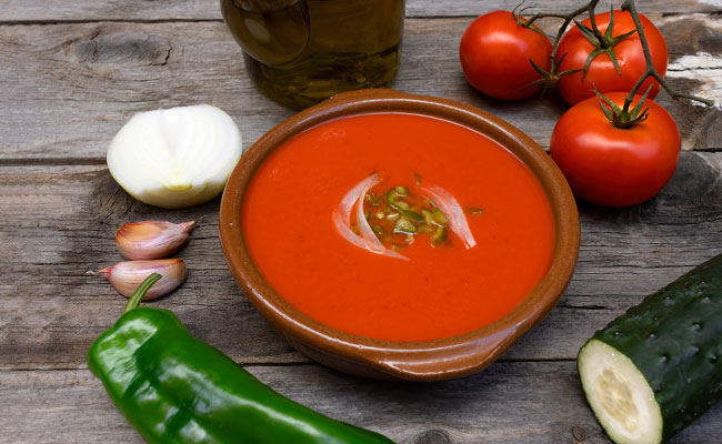 plato de gazpacho acompañado con pepino, ajo y cebolla