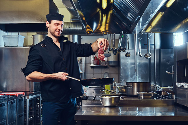 chef condimentando carne mientras la cocina a la sartén