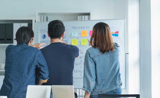 un equipo de trabajo en una reunidos donde se vean alguna pizarra de fondo con gráficos o post it