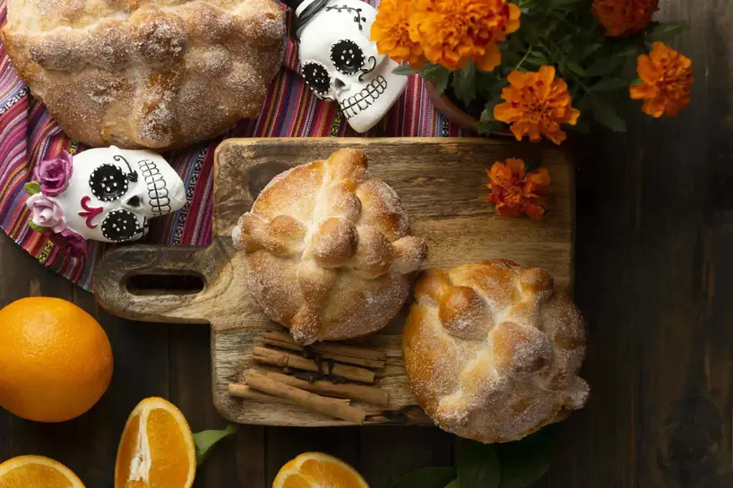 bollos de panes apoyados sobre tabla de madera con calaveras de decoracion