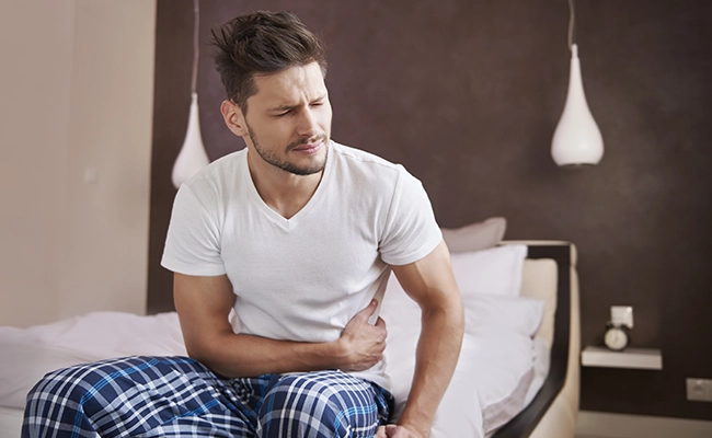 hombre sentado en la cama con dolor estomacal