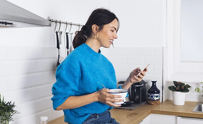 joven utilizando su celular en la cocina de su casa