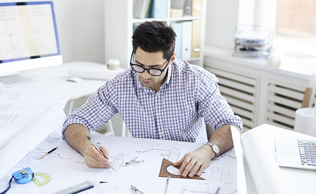hombre trabajando en su escritorio con planos de casas a su alrededor